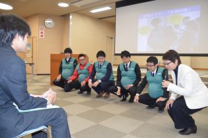 妊婦ジャケットを着用しペンを拾う動作をするJA職員たち
