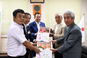 モモを東松島市へ託す生産者（右）