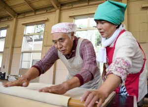 サークル会員(右)と協力し生地を伸ばす参加者(左)