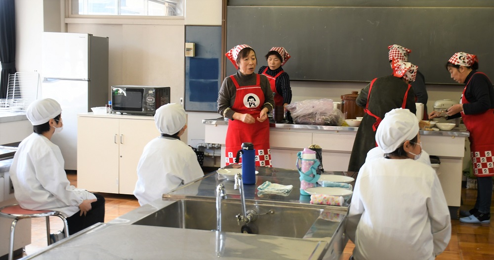 女性部が説明するおにぎりの握り方を真剣に聞く児童